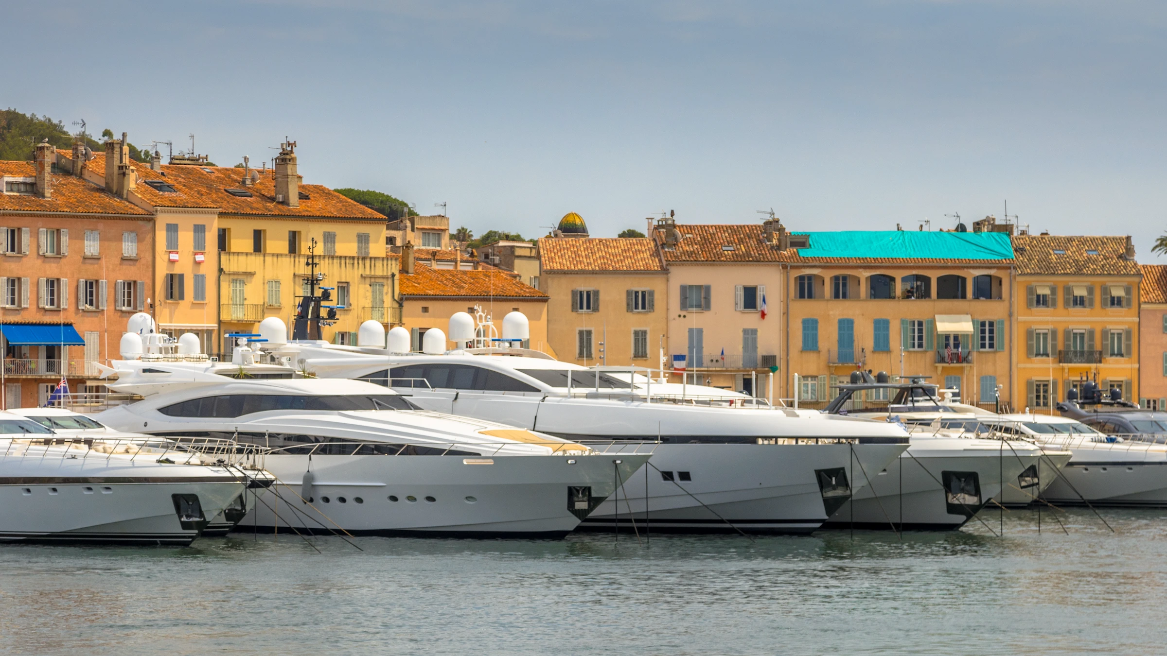 Luxury yachts on the ocean in front of colourful houses in Saint Tropez, French Riviera